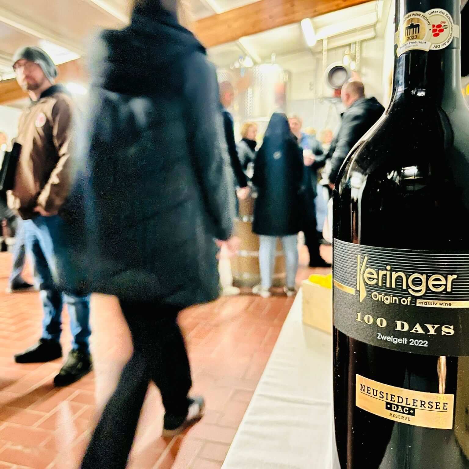 100 DAYS Zweigelt 2022 Flaschenfoto mit Gästen im Hintergrund, Weingut Keringer
